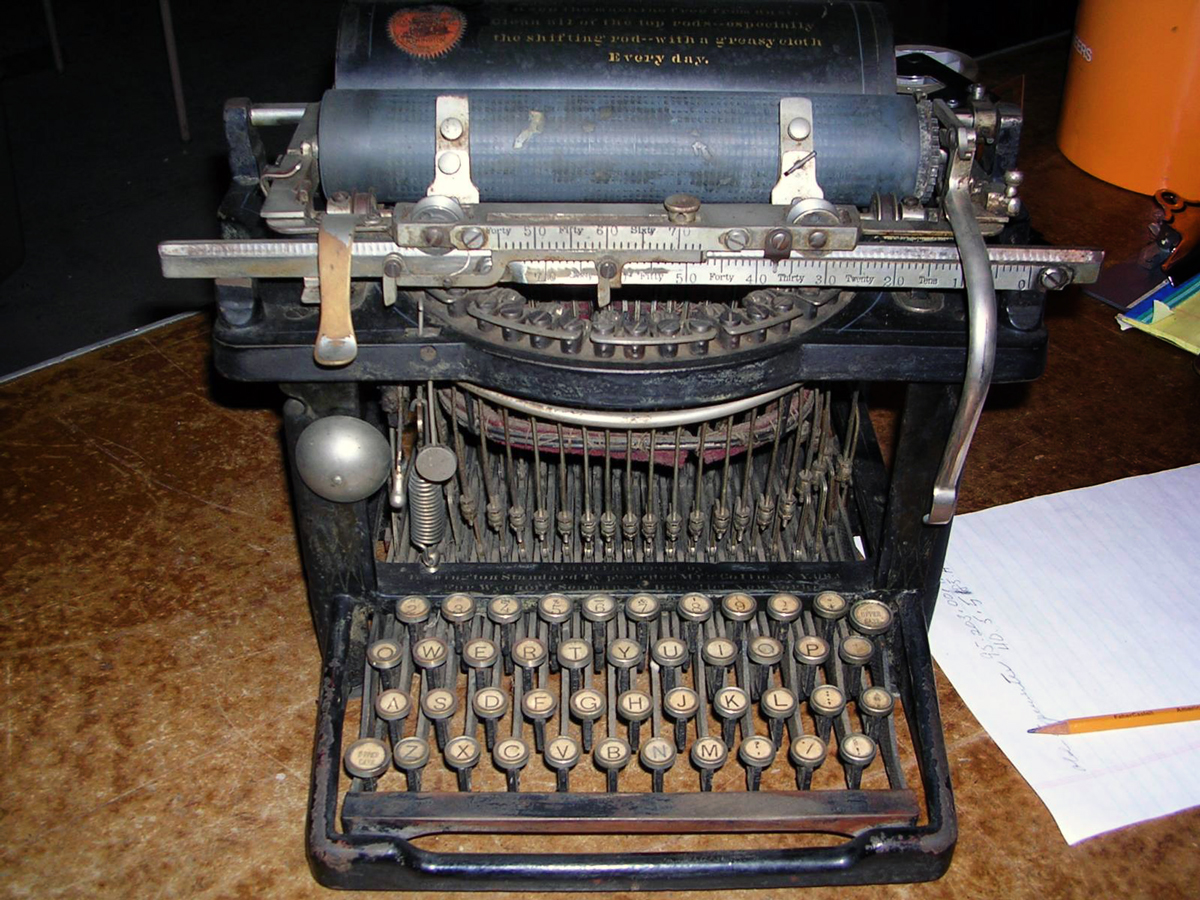 Antique mechanical typewriter with round keys and exposed typebars, showing heavy wear and aging