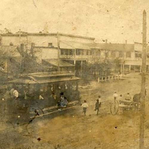 Historic street scene with a horse-drawn streetcar, pedestrians, and two-story buildings in a 19th-century town