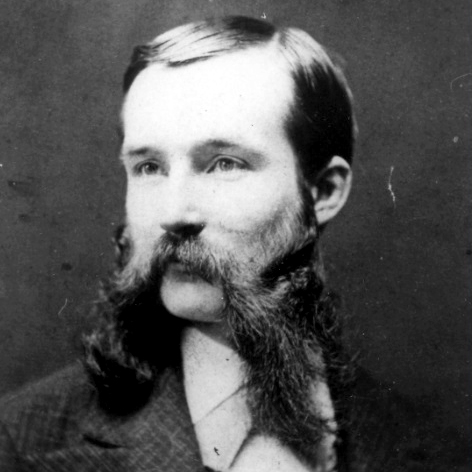 Black and white portrait of a man with a full beard and mustache, wearing a suit jacket