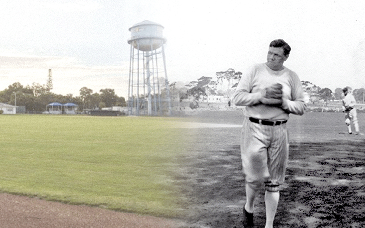 Baseball player in uniform holding a ball on a field, with a water tower and green outfield in the background