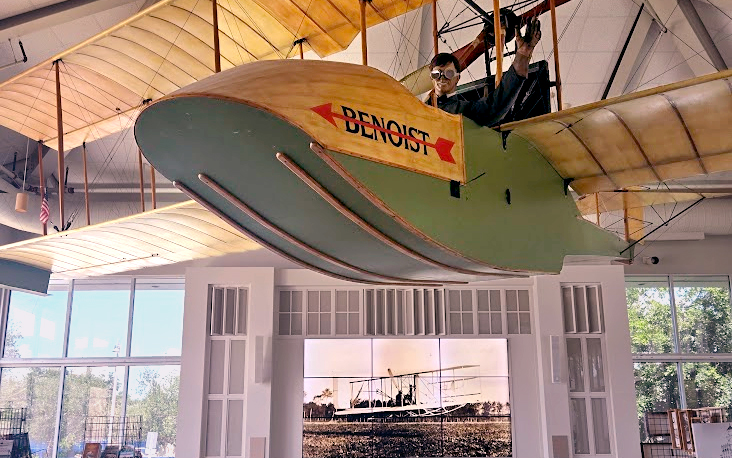 Replica of the Benoist airboat suspended from the ceiling of a museum, with a mannequin pilot in the cockpit