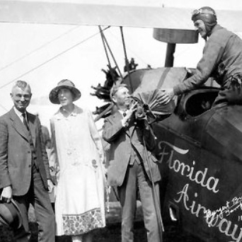 Three people standing beside a biplane marked Florida Airways, with a pilot seated in the cockpit, circa 1920s