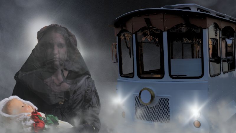 A ghostly cloaked figure holding a baby doll emerges from fog beside a trolley, evoking a haunted tour experience
