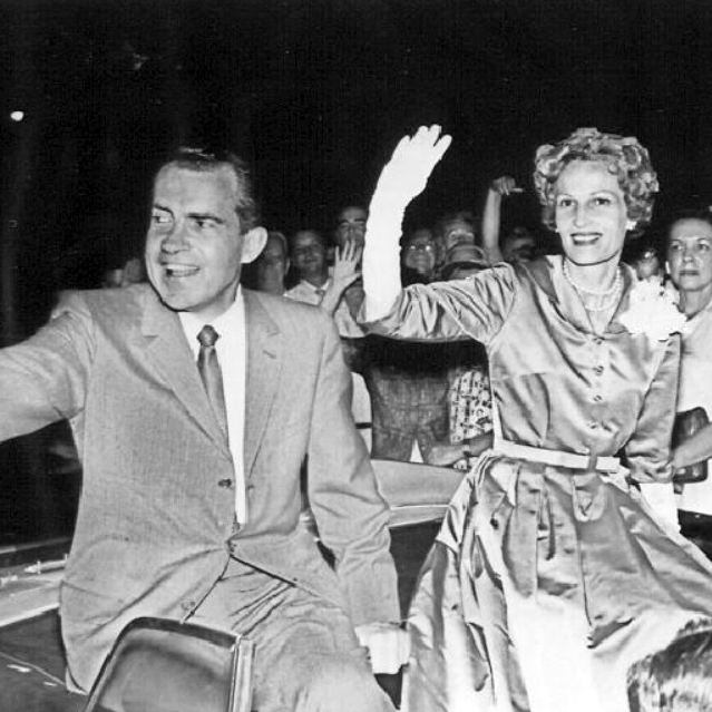 Richard Nixon and Pat Nixon waving to a crowd from an open car, with supporters visible in the background