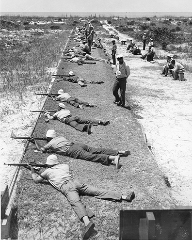 Soldiers lying prone in a line on a firing range, aiming rifles downrange during a marksmanship training exercise
