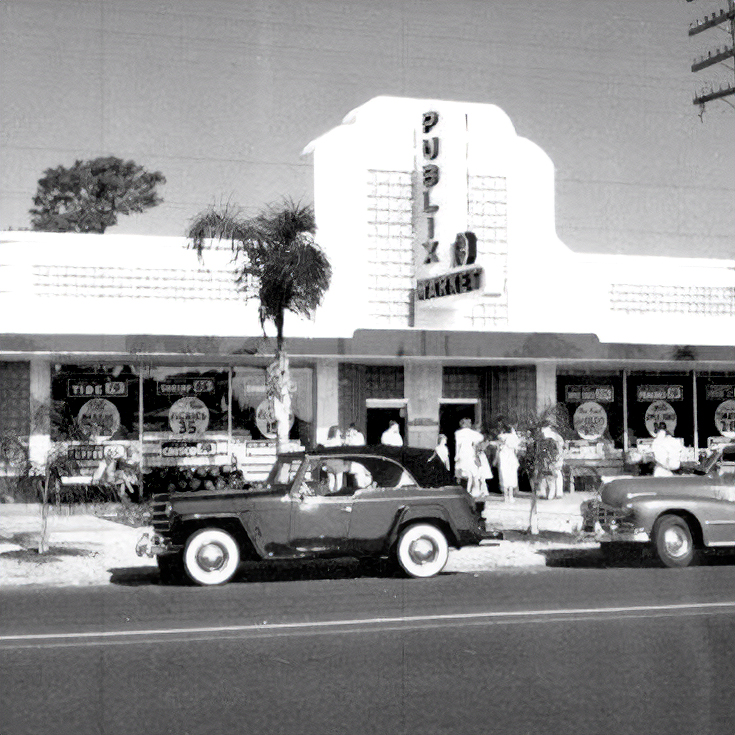 Vintage black-and-white photo of an early Publix Market storefront with classic cars parked outside and shoppers near the entrance