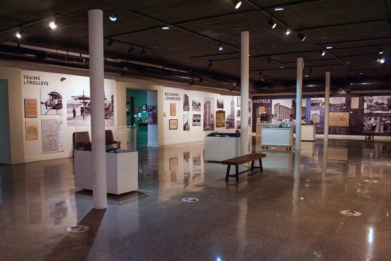 Museum exhibit hall with sections on Trains & Trolleys, Buildings & Churches, and Hotels, featuring historical photos and display cases