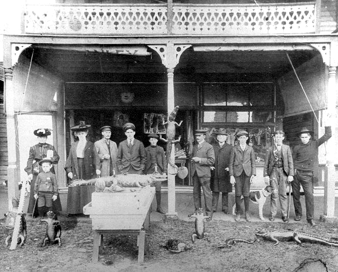 Group of people posing outside a storefront with alligators and reptiles on display, early 20th century black-and-white photo