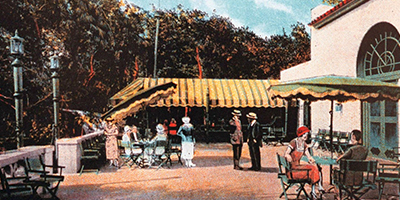 Vintage illustration of an outdoor café terrace with guests seated and standing beneath yellow-striped awnings, surrounded by trees