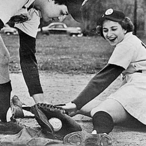 Vintage black-and-white photo of a female baseball player sliding into base, laughing, as another player attempts a tag