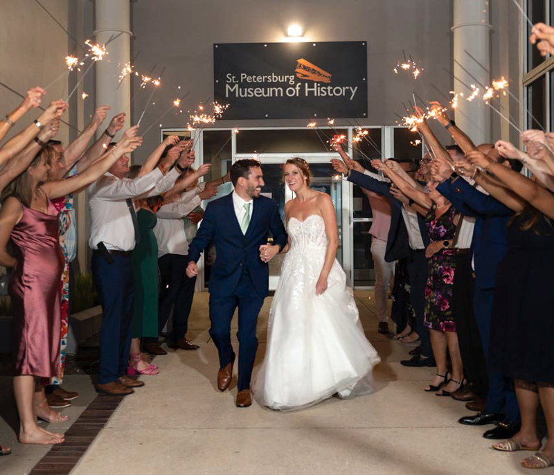 Newlyweds exit the St. Petersburg Museum of History through a sparkler tunnel formed by smiling wedding guests at night
