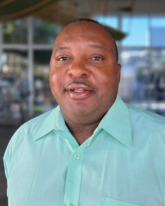 Levi Harris in a light green button-up shirt smiling outdoors with a blurred building in the background