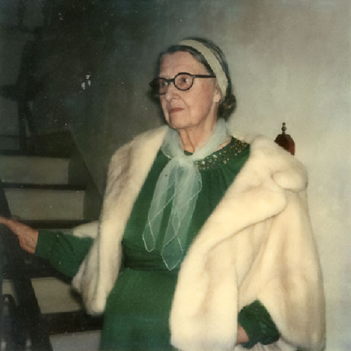 Photograph of Polly Knipp Hill wearing a green dress with neck scarf and white fur coat