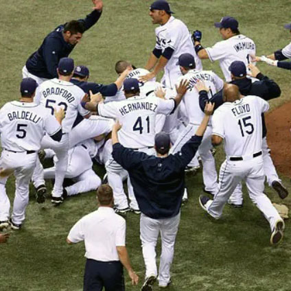 Several baseball players in white uniforms all running to a central spot on the baseball field