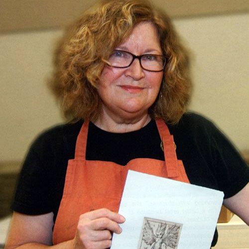 Photo of artist, Holly Bird, a women with curly red shoulder-length hair, holding a print