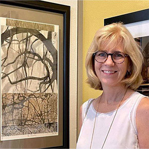 Photo of Mary-Helen Horne standing next to one of her prints with what appear to be tree branches