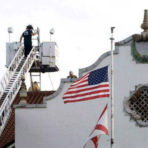 A firefighter is on a ladder truck extended up to the roof of St. Petersburg High School with the American and Florda state flags in the foreground