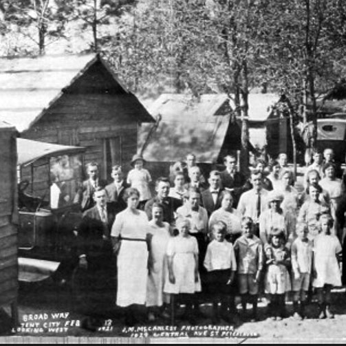 Old black-and-white photo of people standing in front of simple cabins as part of 