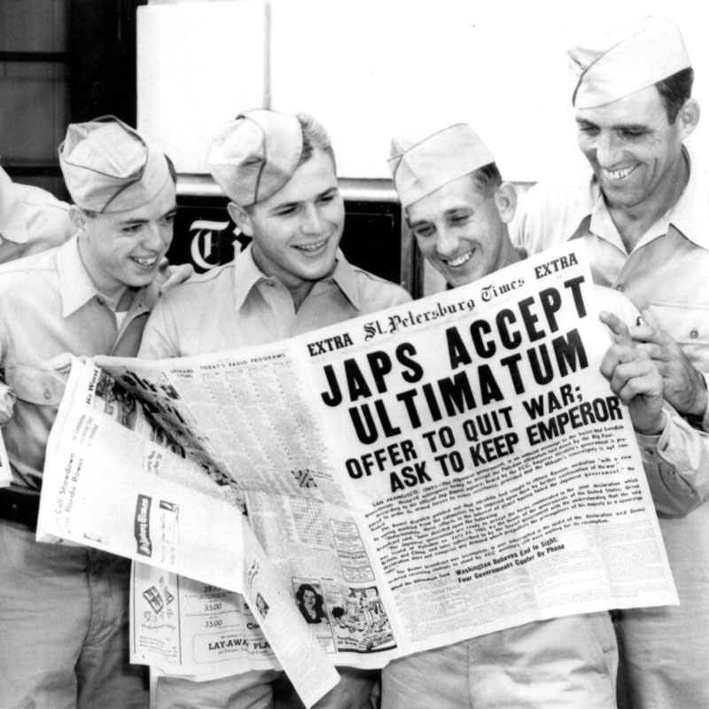 Young men in military uniforms read a newspaper with the headline 