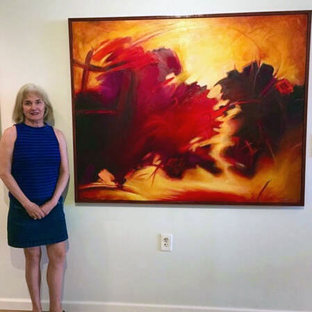 Artist Neverne Covington wears a blue dress while standing next to one of her expressive art pieces in reds and golds