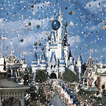 Aerial view of the castle in Magic Kingdom with people marching in a parade and balloons floating up to the sky