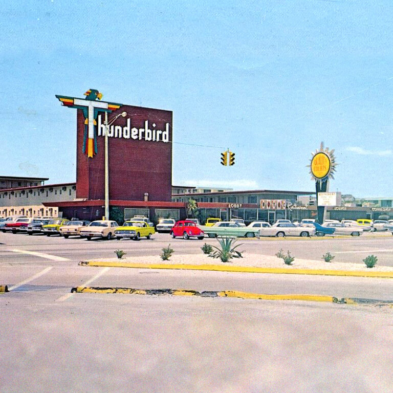 A historic photo of the Thunderbird Motel, a large square red sign marking the lobby, with a parking lot in the foreground filled with cars from the 1950s and early 60s.
