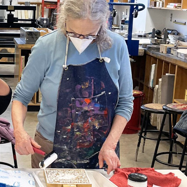 Artist Sherry Smith stands over a print block as she inks it in preparation for printing