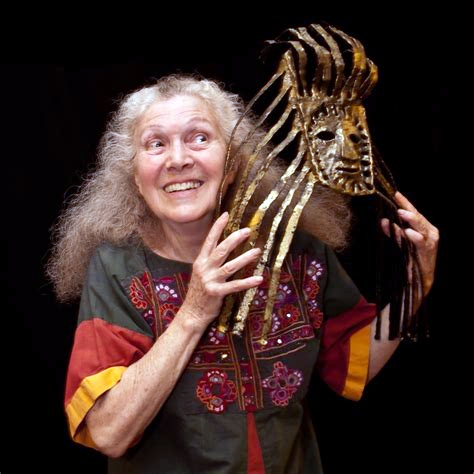 Artist Suzanne Benton smiles as she holds a mask, which appears to be made of metal with wavy edges) in front of her face.