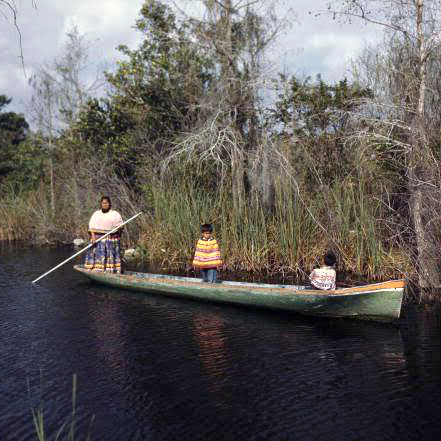 A Seminole family navigates a waterway aboard a dugout canoe