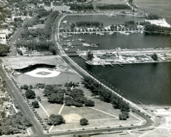 Aerial black-and-white photo of a coastal city with a baseball stadium, marina, and waterfront park