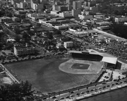 Aerial black-and-white photo of a baseball stadium surrounded by urban buildings and parking lots