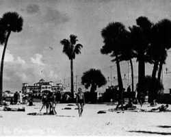 Sunbathers lounge on Spa Beach. Million Dollar Pier in background. c. 1930. Vintage black-and-white photo of Spa Beach, St. Petersburg, Florida, with beachgoers and tall palm trees