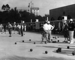 People playing lawn bowls on an outdoor green, with the Pennsylvania Hotel visible in the background, in a vintage black-and-white photo