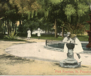 Williams Park, "Park Fountain," two children right foreground around drnking fountain, view of part of fountain right mid-foreground, two adults strolling under trees in background, hand-painted. c. 1917.