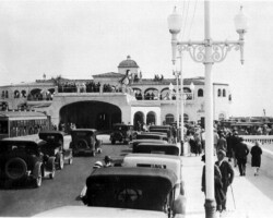 West entrance of the Million Dollar Pier, with a trolley approaching its terminal. A large crowd gathers. c. 1925
