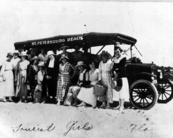Group of women posing in front of a St. Petersburg Beach bus on sandy ground; handwritten caption reads Tourist Girls Fla