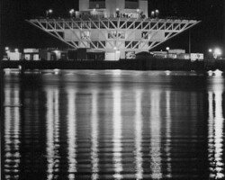 Illuminated modernist building at night reflected in calm water below, black and white photograph