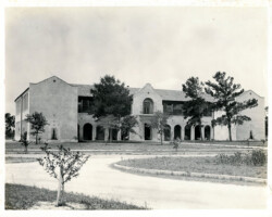 Historic black-and-white photo of a two-story Spanish Colonial Revival building with arched colonnade, surrounded by trees and a curved driveway