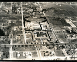 Aerial black-and-white photograph of a campus or institutional complex surrounded by tree-lined streets and open land