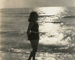 Black and white photograph of a woman wading at the shore. Date unknown, maybe 1960s.