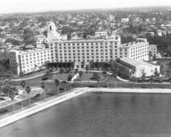 Aerial view of the Vinoy Hotel, c. 1935. Looking north from the Vinoy Basin. Aerial black-and-white photo of a large historic hotel with manicured grounds and palm trees along a waterfront, surrounded by a residential neighborhood